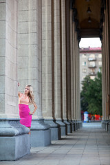 Beautiful woman in pink dress among columns.