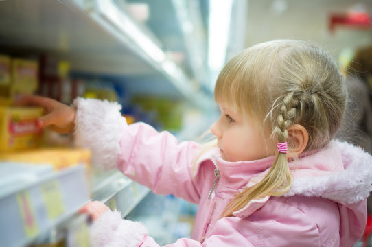 Adorable girl in pink select products on shelves in supermarket
