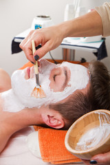 Therapist applying a face mask to a beautiful young man in a spa