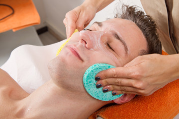 Female hands cleaning man's face  in a spa center