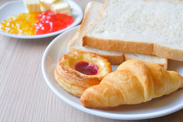 Various breads and Croissants with Jams on breakfast table.