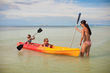 Young mother and two her little daughters kayaking at blue warm