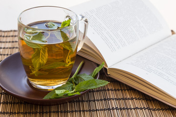 Green tea and leaves of mint in a glass cup with a book