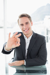 Fototapeta premium Smiling businessman gesturing okay sign at office desk