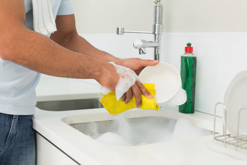Mid section of man doing the dishes at kitchen sink