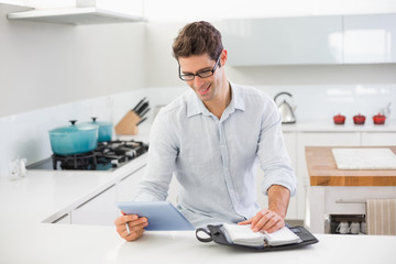 Casual man with digital tablet and diary in kitchen