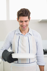 Fototapeta premium Smiling man holding a baking dish in kitchen