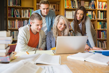 Happy students using laptop at desk in library