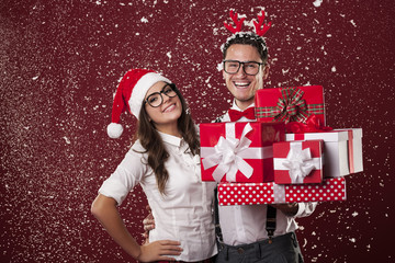 Smiling nerd couple with a lot of christmas presents - obrazy, fototapety, plakaty