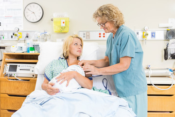 Smiling Nurse Assisting Woman In Breast Feeding Baby In Hospital
