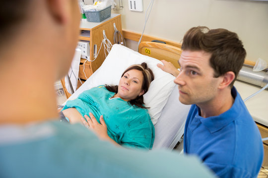 Pregnant Woman And Husband Looking At Nurse In Hospital