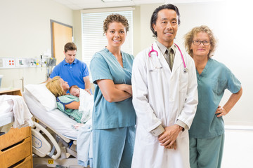 Confident Medical Team With Newborn Baby And Parents In Backgrou