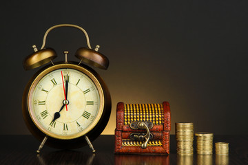 Antique clock and coins on wooden table on dark color