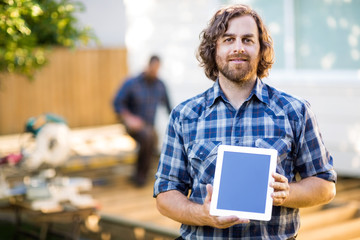 Carpenter Displaying Tablet Computer With Coworker Working In Ba