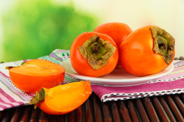 Ripe persimmons on plate on table on bright background