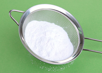 Powdered sugar in metal sieve on green background
