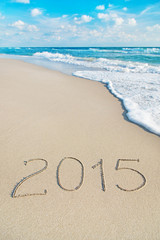 inscription 2015 on sea sand beach with the sun rays against wav