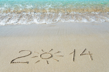 inscription 2014 on sea sand beach with the sun rays against wav