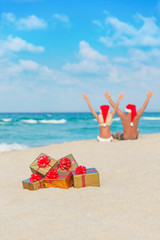 Fototapeta na wymiar happy couple in santa hats hands up at sea beach with christmas