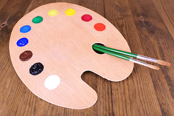 Wooden art palette with paint and brushes on table close-up