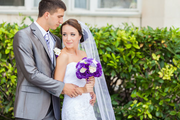 young bride and groom standing outdoors hugging and smiling