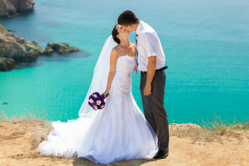 wedding couple stands on a cliff, blue sea on background