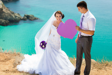 wedding couple stands on a cliff, blue sea on background