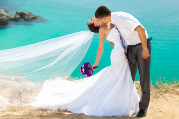 wedding couple stands on a cliff, blue sea on background