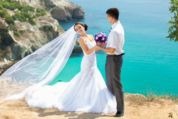 wedding couple stands on a cliff, blue sea on background