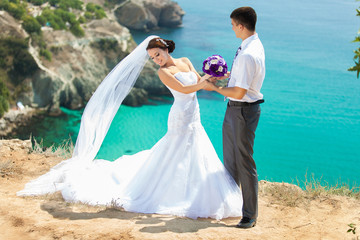 wedding couple stands on a cliff, blue sea on background