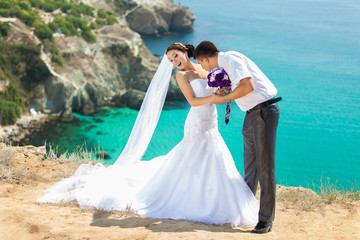 Fototapeta na wymiar wedding couple stands on a cliff, blue sea on background