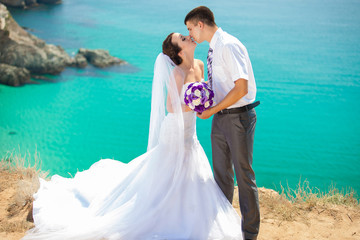 wedding couple stands on a cliff, blue sea on background