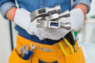 Fototapeta na wymiar Mid section of handyman holding hammers with toolbelt around wai