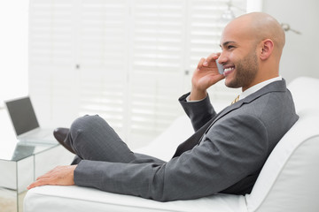 Smiling elegant businessman using cellphone on sofa at home