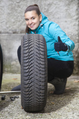 Fototapeta na wymiar Smiling girl showing OK sign whilst replacing summer tyres