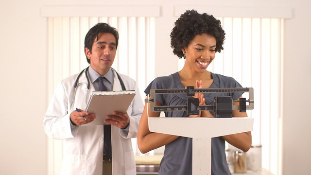 African American woman checking weight with doctor