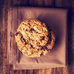 Stacked chocolate chip cookies on brown napkin over wooden backg