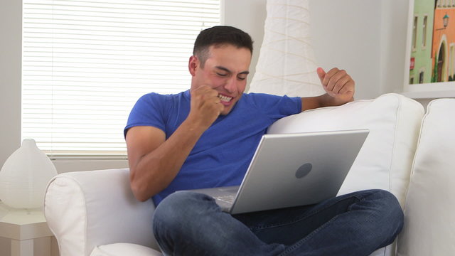 Cheering Hispanic man watching sports on laptop computer