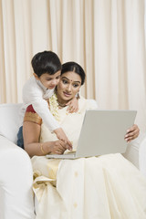 Woman using a laptop with her son standing behind her