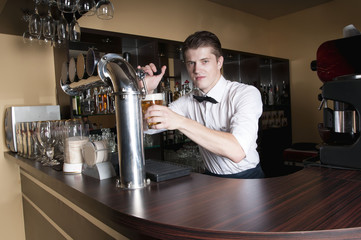 Bartender in white shirt serving beer in front of the bar.