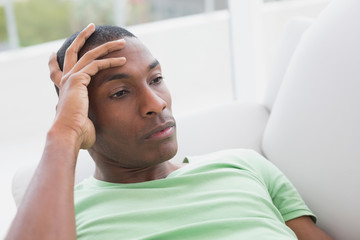 Thoughtful relaxed young Afro man lying on sofa