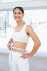 Fototapeta na wymiar Smiling woman measuring waist in fitness studio