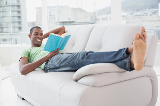 Full length of smiling Afro man reading a book on sofa