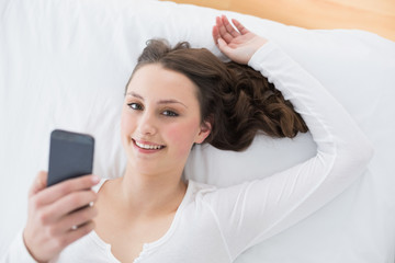 Young brunette with mobile phone in bed