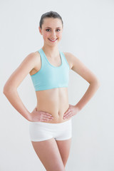 Obraz premium Smiling toned woman with hands on hips against wall