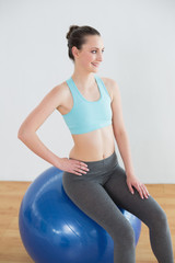 Smiling fit woman on exercise ball in fitness studio