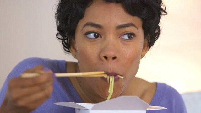 Black woman eating noodles from Chinese takeout