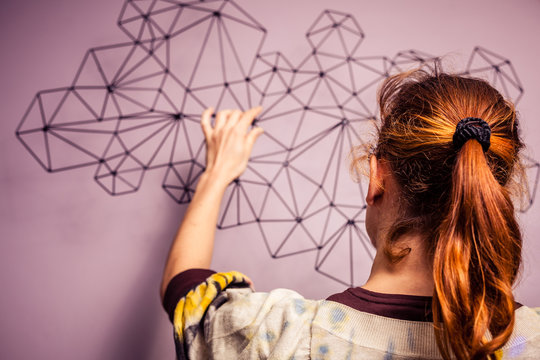 Young Woman Hanging A Piece Of Art On Her Wall