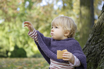 little girl eating a biscuit , outdoors in the park
