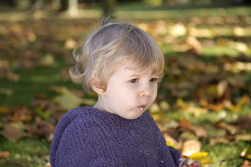 little girl eating a biscuit , outdoors in an autumn park